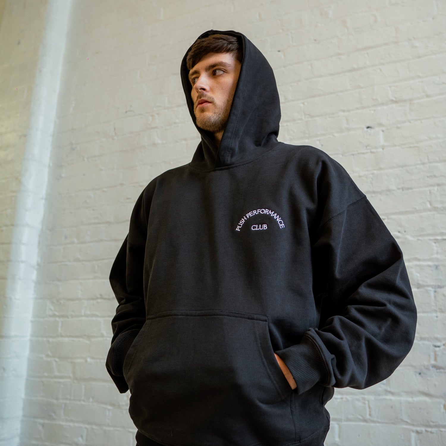 Close-up of premium cotton fabric, oversized hood, and subtle Push Performance branding on black Essential Warm Up Hoodie