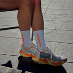 white/orange socks worn by a runner sat down, wearing matching running shoes. 