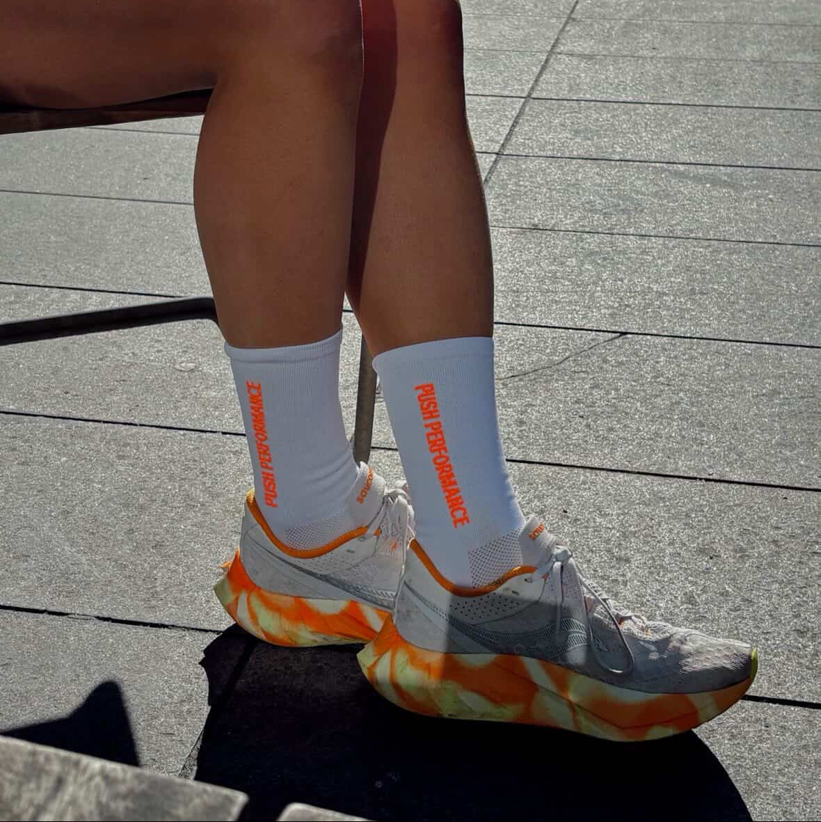 white/orange socks worn by a runner sat down, wearing matching running shoes. 