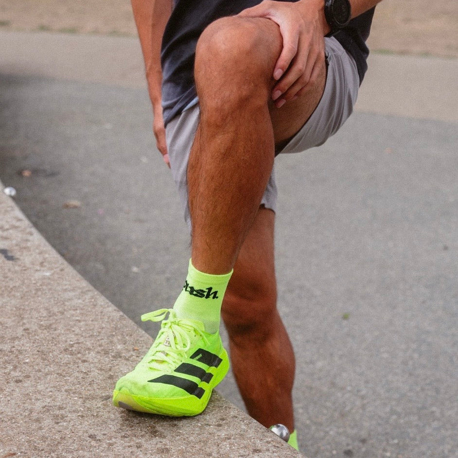 A close-up of a person wearing bright neon yellow push performance running socks.