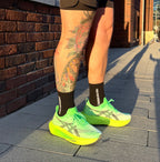 Person wearing bright green running shoes and black performance running socks with tattoos on legs. 