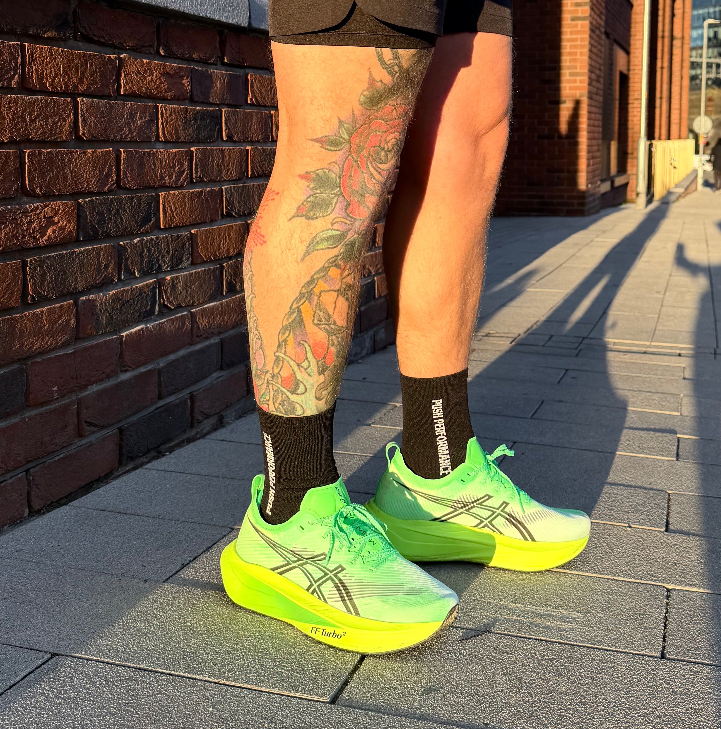 Person wearing bright green running shoes and black performance running socks with tattoos on legs. 