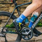 Cyclist on a bike with focus on the chain and gear area, wearing blue socks with branding.