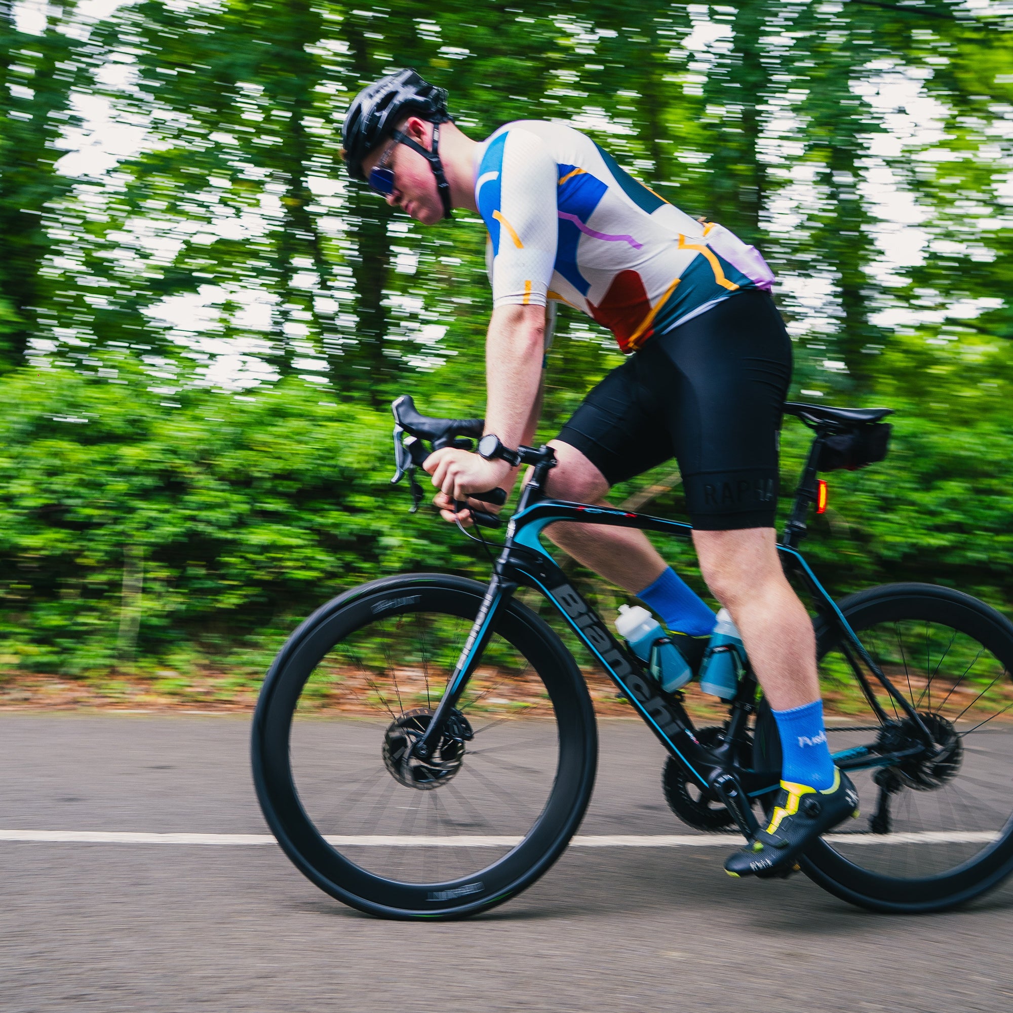 Cyclist in a colorful outfit riding a black bicycle on a road with greenery in the background