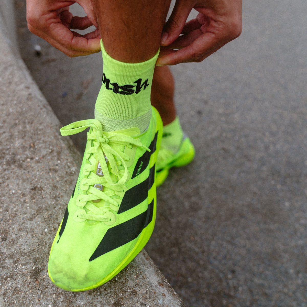 A close-up of a person pulling up bright neon yellow push performance running socks.