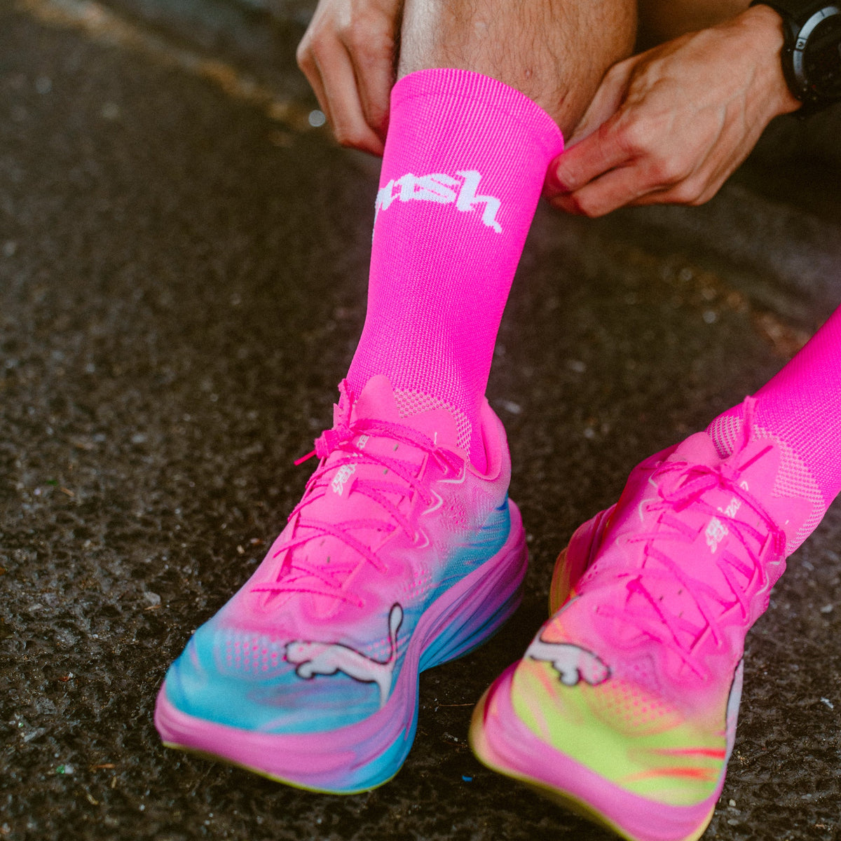 A close-up of a person pulling up bright neon pink push performance running socks.