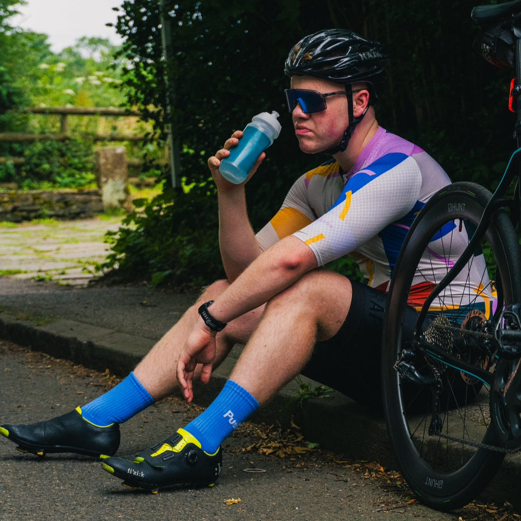 Cyclist taking a break, sitting on the side of a road, holding a water bottle.