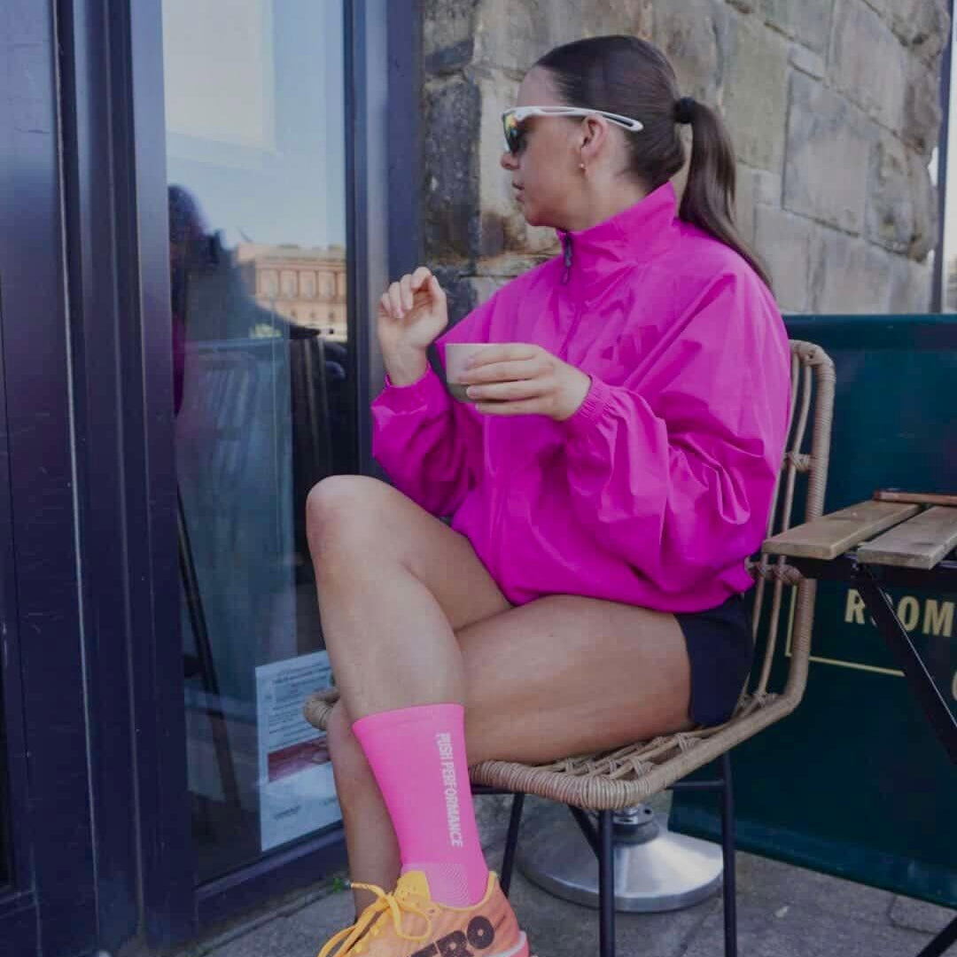 runner wearing bright pink running socks and running jacket with a coffee in hand 