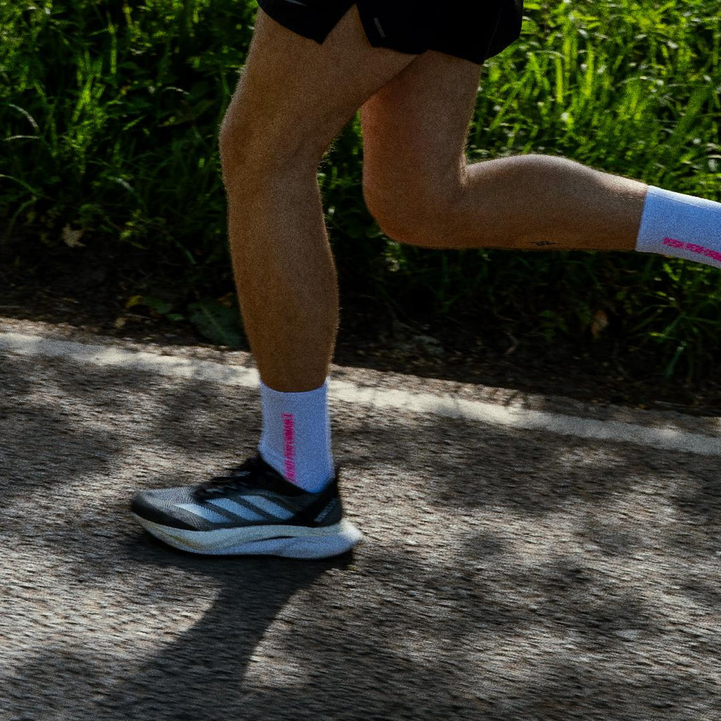 Person running on a road with grass in the background in white and pink performance running socks. 