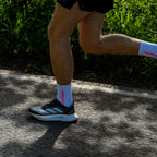 Person running on a road with grass in the background in white and pink performance running socks. 